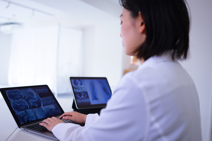 Female doctor using a laptop and looking at screens of Magnetic Resonance Imaging.