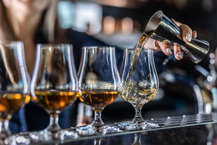 Photo shows a bartender pouring liquor from steel jigger into glass at bar/Getty Images