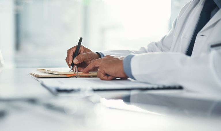 Photo shows doctor writing on paper attached to a clipboard/Getty Images